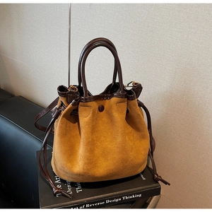 Détail du sac seau en daim caramel avec fermeture à cordon et poignées en cuir contrasté