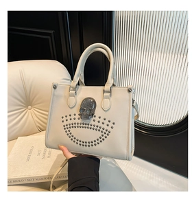 Gros plan du sac fourre-tout beige orné d'un crâne métallique et de clous argentés