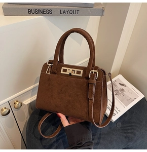 Detail of dark brown suede handbag featuring golden twist lock and refined stitching