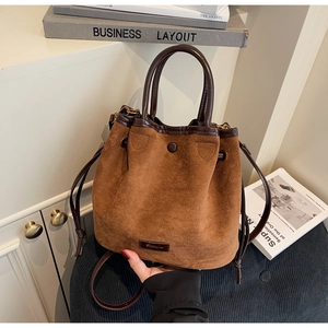 Détail du sac seau en daim caramel avec bandoulière en cuir et plaque logo métallique