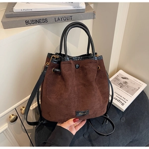 Détail du sac seau en daim marron avec anses en cuir noir et étiquette logo