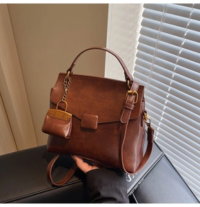 Close-up of vintage brown PU leather handbag with golden hardware and small charm pouch