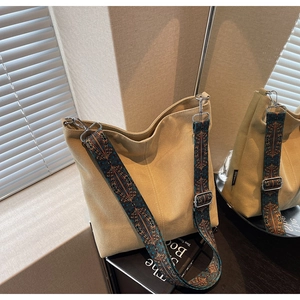 Close-up of khaki canvas bucket bag with wide geometric pattern strap and silver metal buckle