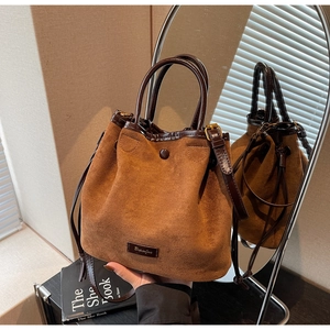 Détail d'un sac seau en daim marron avec garniture en cuir, cordon et logo métallique