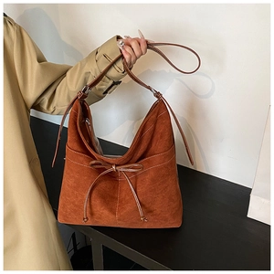 Detail of a brown suede hobo bag featuring white stitching and bow tie decoration