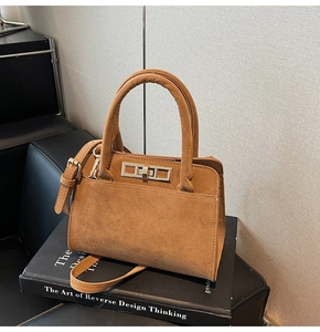 Detail of caramel brown suede handbag with silver metal twist lock on a black book