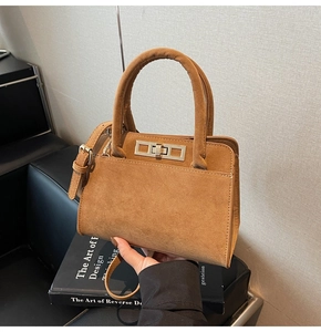 Detailed view of tan suede handbag with metal twist lock and cylindrical top handle