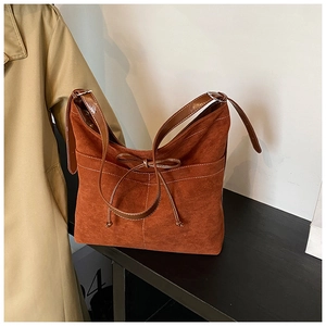 Détail du sac cabas en daim marron caramel avec nœud fin et surpiqûres blanches contrastées