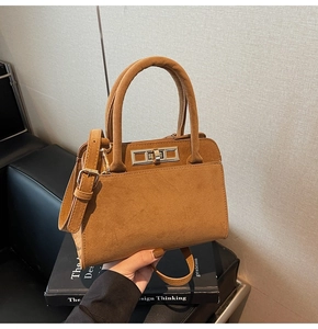Detail of a brown suede handbag featuring a silver rectangular twist lock and top handle