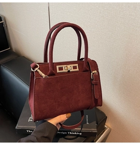 Close-up of a burgundy suede handbag featuring golden twist lock and twin handles