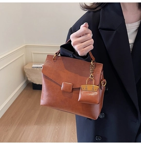 Detail view of retro caramel square handbag with decorative mini bag charm and metal ring