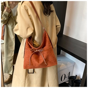 Détail du sac bandoulière en daim marron rouge avec nœud en cuir et coutures blanches