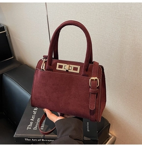 Detail view of burgundy faux suede handbag with gold lock and sleek adjustable strap