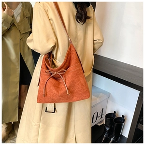 Détail du sac bandoulière mat rouge rouille avec nœud et surpiqûres sur un trench-coat