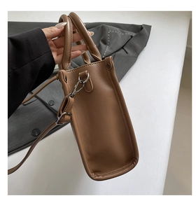 Détail de la texture cuir marron, de la couture latérale et de l'anneau en D du sac
