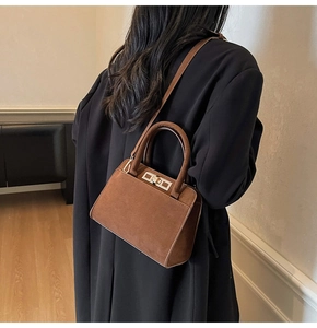 Side view of dark brown suede handbag with golden metal lock worn by a female model