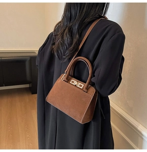 Detail showing the brown suede texture and golden metal rotary lock of the handbag