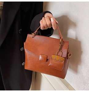 Detail of caramel brown PU leather handbag featuring a mini briefcase charm accessory