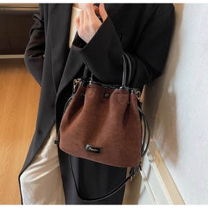 Vue latérale d'un sac seau en daim marron porté par un mannequin en blazer noir
