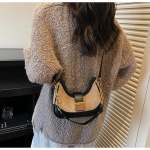 Detail of color-blocked leather underarm bag with gold chain strap on knitted sweater