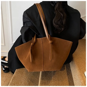 Detail of a brown suede tote bag featuring unique knot designs on the shoulder straps