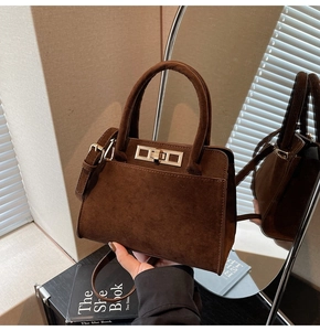 Detailed view of deep brown suede handbag with metal turn-lock and dual handles
