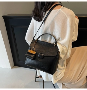 Detail view of black leather handbag with a miniature orange charm and flap closure
