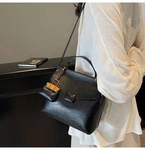 Detail of glossy black textured leather handbag featuring a stylish miniature charm