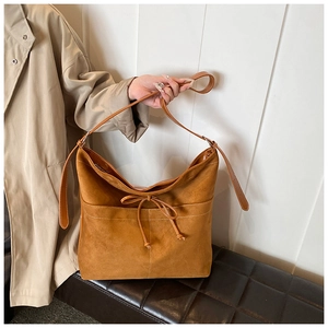Detail of caramel suede tote bag featuring white stitching and bow drawstring design