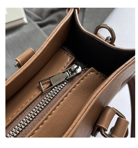 Détail du sac en cuir marron avec fermeture éclair argentée vintage et anneau en D