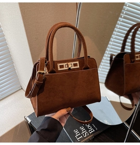 Detailed view of dark brown suede handbag with a gold metal lock and leather handles