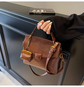 Detail view of brown vintage satchel bag with hard handle and mini pouch charm attachment