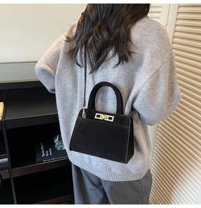 Rear view of a model carrying a black suede tote bag with a golden metal twist lock