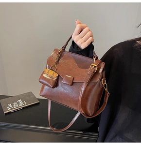 Close-up of brown glossy handbag with vintage gold buckles and a mini charm pouch