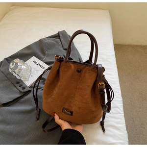 Détail du sac seau en daim avec bordures en cuir marron et bandoulière réglable