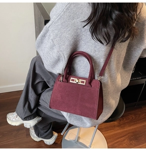 Detailed close-up of a burgundy suede handbag featuring a gold metallic twist lock closure