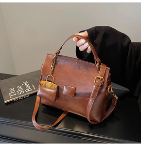 Close-up of brown vintage handbag featuring a mini bag charm and bronze metal hardware