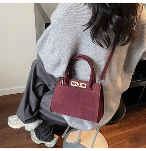 Detail of burgundy faux suede handbag with gold lock on a model showing commuters style