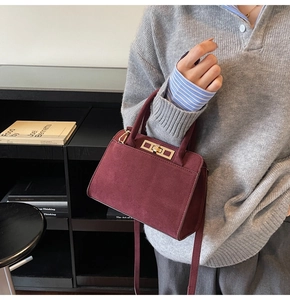 Detail of burgundy suede tote bag featuring a gold metal buckle and leather shoulder strap