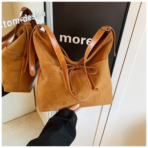 Détail d'un sac cabas marron en daim avec nœud décoratif et surpiqûres blanches contrastées