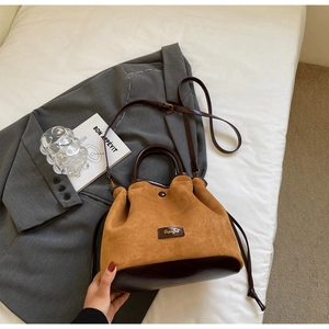 Détail du sac seau bicolore en daim et cuir avec cordon de serrage et logo en métal