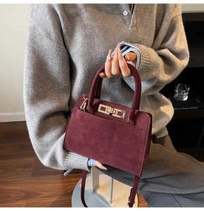 Detailed macro view of Burgundy suede handbag with golden metal twist lock and top handle