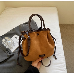 Vue de dessus d'un sac seau vintage en daim marron posé sur une literie blanche épurée