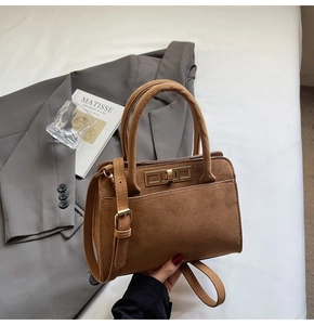 Detail of a brown suede handbag featuring a gold rectangle turn-lock and adjustable strap