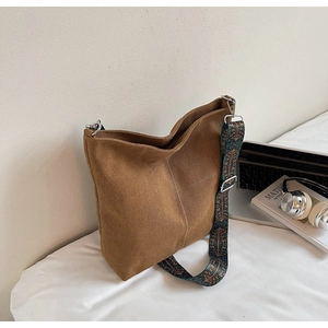 Brown canvas hobo bag with vintage printed strap next to a laptop and headphones
