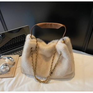 Detail of plush faux fur tote with leather handles and gold chain strap on office desk
