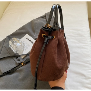 Vue détaillée du sac seau en daim marron foncé avec anse noire et accents métalliques dorés