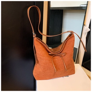 Détail d'un sac seau en daim avec nœud décoratif et bandoulière en cuir réglable