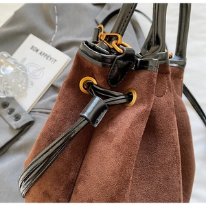 Détail du sac seau en daim marron avec garniture en cuir noir et œillets en métal doré