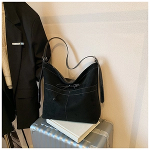Détail du sac hobo en daim noir avec coutures contrastées blanches et nœud décoratif